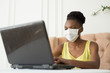 © Alexandr - beautiful young african woman sitting in a chair with a laptop in a medical mask