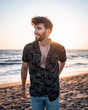 Charming man in casual clothing smiling. Handsome guy standing alone on the beach in sunset and smiling.