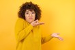 © Roquillo - Beautiful Arab businesswoman pointing aside with both hands showing something strange and saying: I don't know what is this. Standing against yellow background. Advertisement concept.