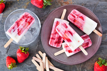 Poster - Strawberry vanilla yogurt ice pops. Top down table scene with a dark stone background.