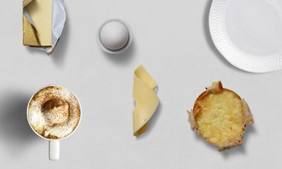 Breakfast table with tea, coffee, eggs, butter, cheese and a plate on a white background