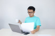 © Reezky - Wow face of Young Asian man shocked what he see in the document when working with laptop. isolated grey background wearing blue shirt.