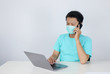 © Reezky - Young Asian Man wearing medical mask is serious and focus when working on a phone and laptop on the table. Indonesian man wearing blue shirt.