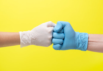 yellow background and hands in medical gloves. hands in latex medical gloves punch each other. one hand in a blue glove and the second hand in a white glove. woman and a man