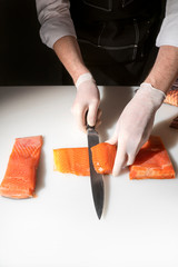 Wall Mural - Chef cook in gloves cuts a salmon fish of a knife on the table