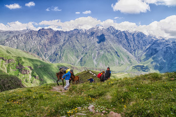 KAZBEGI, GEORGIA - JUNE 23L Men with horses carrying backpacks at Caucasus mountains on June 23, 2013 in Kazbegi, Georgia. They intend to reach Kazbek, third highest mountain in Georgia.