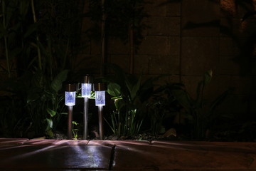 Garden LED lamp lighting. Small solar lighting shining in a garden and casting shadow in multiple direction. cool light temperature for modern hi tech landscape design.