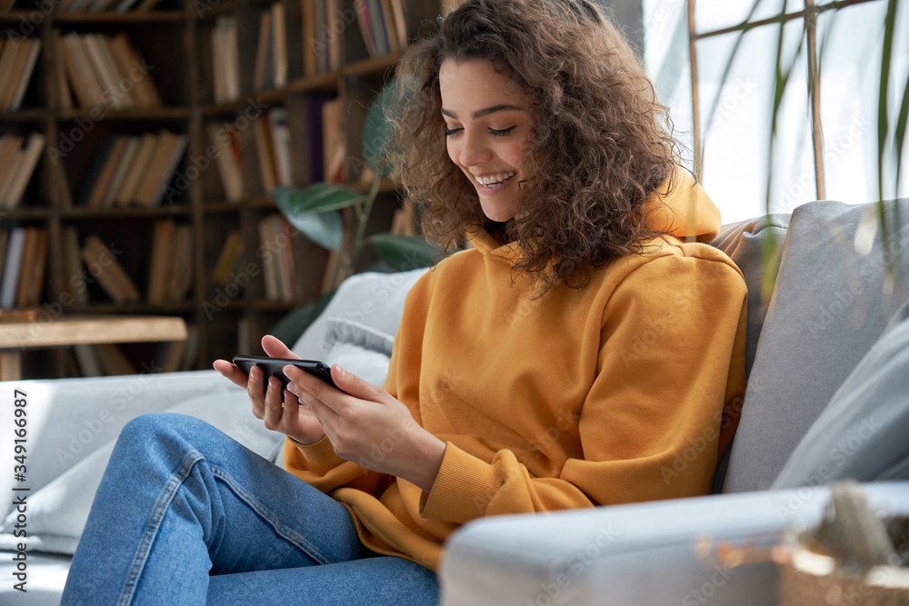 Happy young hispanic latin teen girl sit on sofa at home holding phone ...