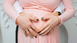 © Red Cristal - Pregnant Belly with fingers Heart symbol. Beautiful Young Pregnant Woman and Her Husband Together Caressing Her Pregnant Belly. Pregnancy. Love Concept. Mom and Dad waiting for newborn baby. Parents