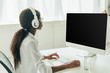 © LIGHTFIELD STUDIOS - Young African American freelancer in wireless headphones looking at computer monitor with blank screen