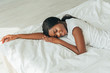 © LIGHTFIELD STUDIOS - high angle view of beautiful, smiling african american girl lying on white bedding with closed eyes