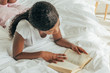 © LIGHTFIELD STUDIOS - overhead view of young african american woman reading book in bed