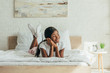 © LIGHTFIELD STUDIOS - happy african american girl lying in bed, smiling and looking away