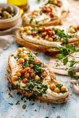 Wall Mural - Vegetarian sandwich with addition hummus spread, fresh chopped parsley, chickpeas and olive oil close up view