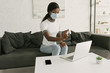 © LIGHTFIELD STUDIOS - young african american freelancer in medical mask spraying antiseptic on laptop