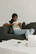 © LIGHTFIELD STUDIOS - young african american freelancer resting on sofa while reading book near table with laptop