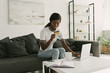 © LIGHTFIELD STUDIOS - Smiling African American girl holding credit card while sitting near table with laptop, notebook and coffee cup