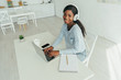 © LIGHTFIELD STUDIOS - high angle view of smiling african american freelancer in wireless headphones working on laptop in kitchen