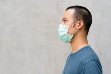 Wall Mural - Closeup profile view of young Asian man with mask for protection from corona virus outbreak outdoors