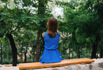 A lonely girl sits in a park alone in the distance from people