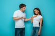 © LIGHTFIELD STUDIOS - young man speaking to offended african american girlfriend touching chest on blue background