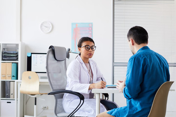 Wall Mural - Female doctor discussing with patient his disease while sitting at the table during his visit at the hospital