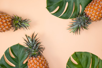  Beautiful pineapple on tropical palm monstera leaves isolated on bright pastel orange pink background, top view, flat lay, overhead above summer fruit.