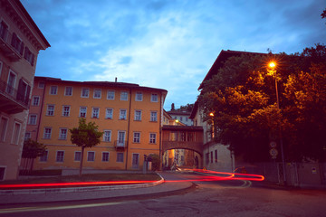 Italian cityscape evening mysterious narrow empty street by night. With car light trace. Night view of the Rovereto city