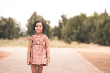 Wall Mural - Smiling cute child girl 4-5 year old wearing stylish dress posing in park outdoors closeup. Summer time. Vacation season.