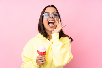 Young brunette girl holding a cornet ice cream over isolated pink background shouting with mouth wide open