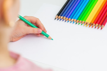 Sticker - Kid girl is drawing with color pencils on white sheet of paper. Copy space for text. Mockup. Selective focus.