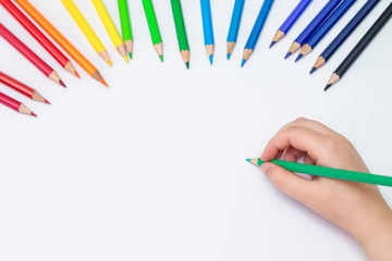 Wall Mural - Top view of baby's hand drawing with green pencil on white paper with the set of colour pencils. Kids painting concept. Copy space for text. Mockup.