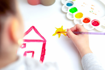 Sticker - Top view of little hand of child drawing house and sun by watercolors. Education and school concept.