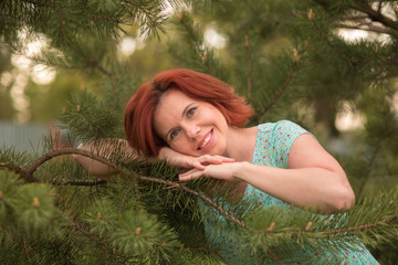 Beautiful young red hair woman in blue dress posing with a pine branch.