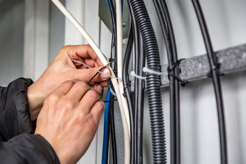 Hands fasten the ties on the cable, which are on the cable tray. Close-up. Horizontal orientation.