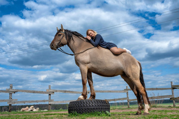 Beautiful young girl rides a horse on a field in summer.