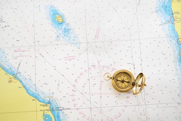 Retro styled golden compass (sundial) and old white nautical chart close-up. Vintage still life. Sailing accessories. Travel and navigation theme