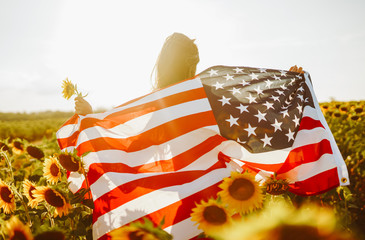 4th of July. Amazing girl in hat with the American flag in a sunflower field. Freedom day. Sunset light. Independence Day. Patriotic concept
