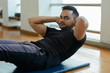 © Ranta Images - Young bearded Indian man doing sit ups on the floor at the gym