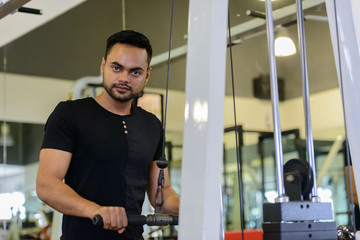 Young bearded Indian man using exercise equipment at the gym