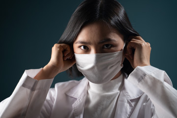 Asian woman in medical uniform wearing protective face mask isolated on blue background. COVID-19, Coronavirus concepts.