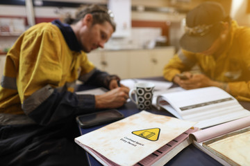 Occupational health and safety confined spaces permit book placing on the table with defocused supervisor writing job hazard analysis risk assessment with teammate prior starting   