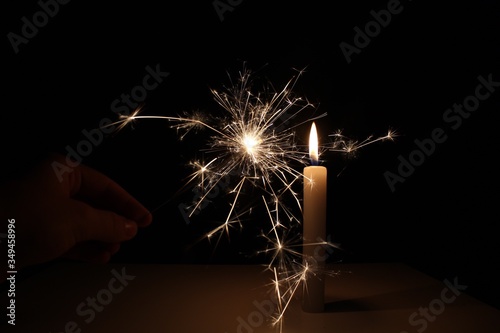 Fotomural Cropped Hand Holding Burning Sparkler By Candle In Darkroom