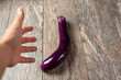 A view of a hand closing in on picking up an eggplant, resting on a wooden surface.