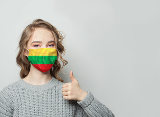 Wall Mural - Happy woman in face mask holding thumb up with Lithuanian  flag background. Flu epidemic and virus protection concept