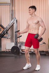 Young man flexing muscles with barbell in gym.