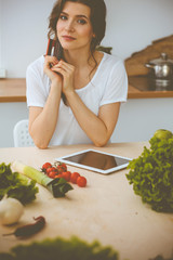 Wall Mural - Young woman looking for a new recipe for cooking in a kitchen. Housewife is making online shopping by tablet computer and credit card