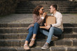 © Aleksandr - Young couple sitting on stairs outdoor and eating pizza. Handsome man with beaufitul woman taste pizza with vegetables. Vegan fast food