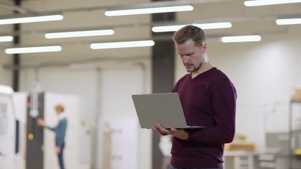 Medium shot of concentrated middle aged male engineer working on laptop computer standing in laboratory, copy space to left