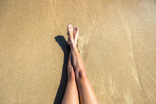 Long Slim Young Woman Legs Relaxing Lying Down And Sunbathing On Sand Tropical Beach Under Hot Sun In Summer. Skincare, Sun Aging Protection And Sea Travel Concept.
